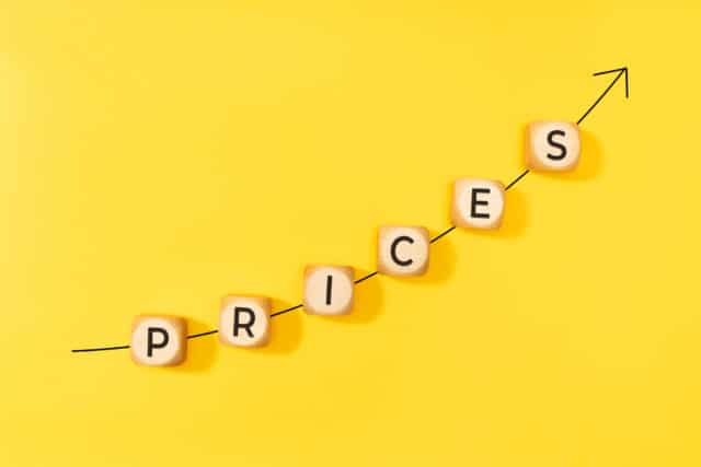 Rising prices concept. Rising arrow and text on wooden blocks on yellow background. Copy space Rising prices are causing rising meeting budgets according to a new survey.