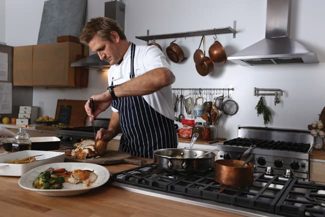 Chef Curtis Stone carving a chicken in a studio kitchen