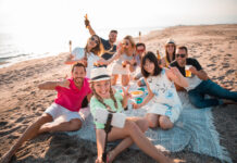Multicultural group of friends partying on the beach – happy young people celebrating during summer vacation, summer time and holidays concepts.