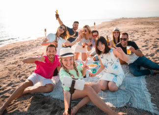 Multicultural group of friends partying on the beach – happy young people celebrating during summer vacation, summer time and holidays concepts.